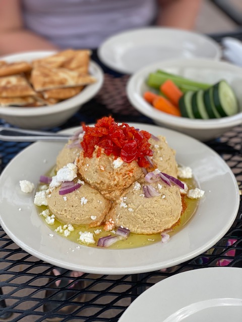 A plate of hummus topped with roasted red peppers and red onions