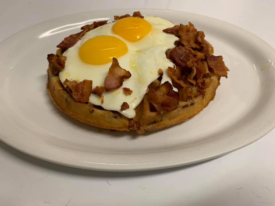 A waffle covered in pieces of bacon topped with two eggs over easy